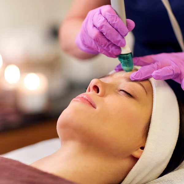people, beauty, cosmetology, exfoliation and technology concept - beautiful young woman having microdermabrasion facial treatment with crystals in spa